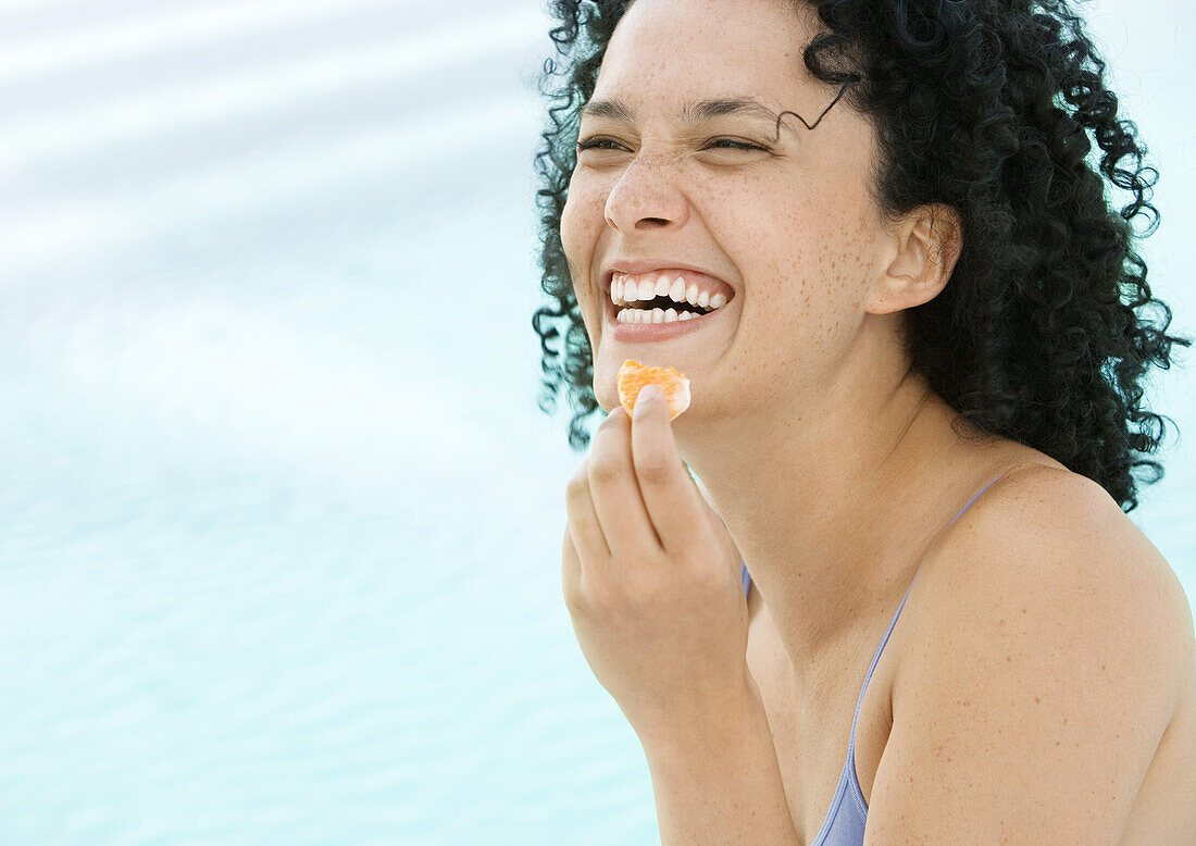 Young woman eating orange and laughing