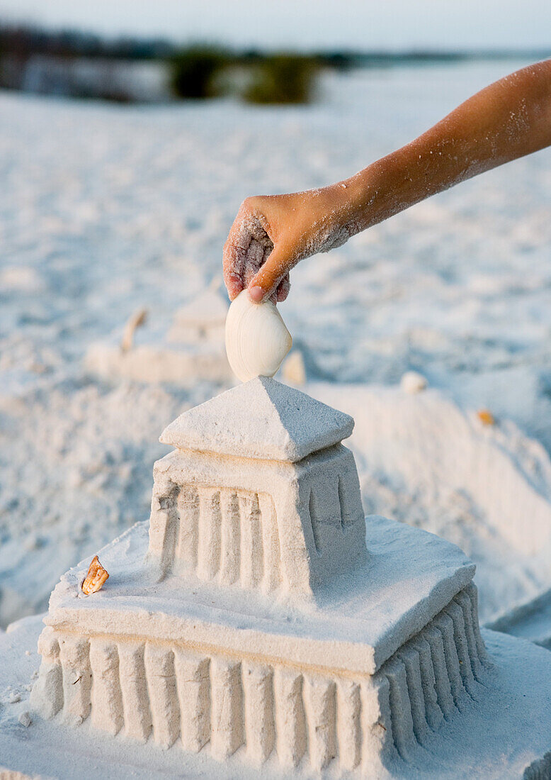 Child placing seashell on top of sand castle