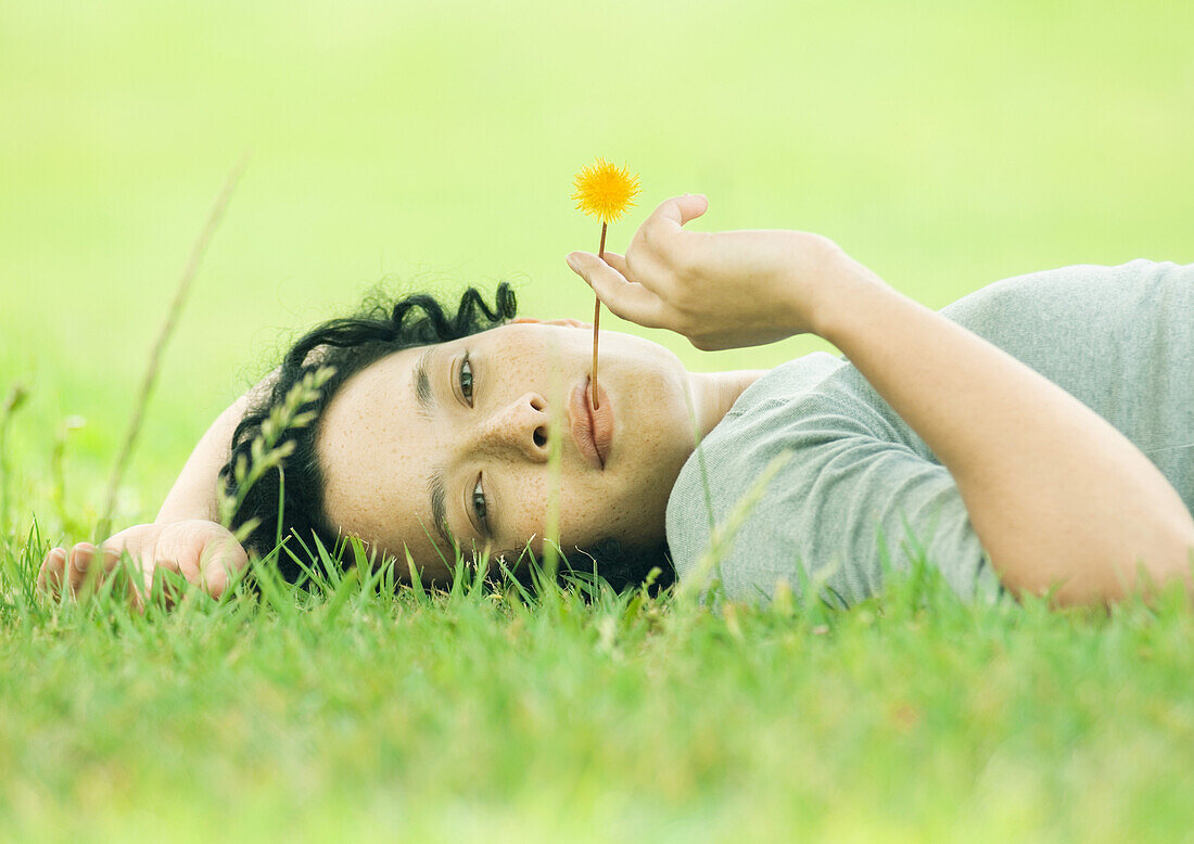 Junge Frau im Gras liegend mit Blume im Mund