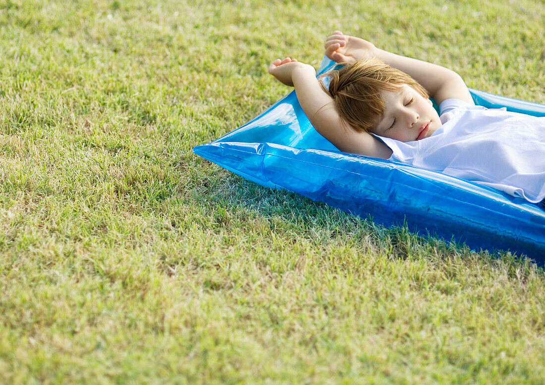 Little boy sleeping on inflatable raft, on grass