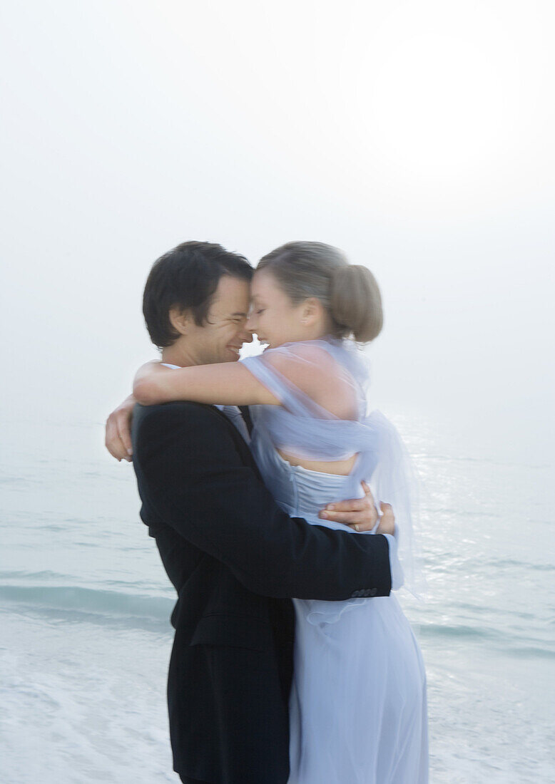 Bride and groom embracing on beach