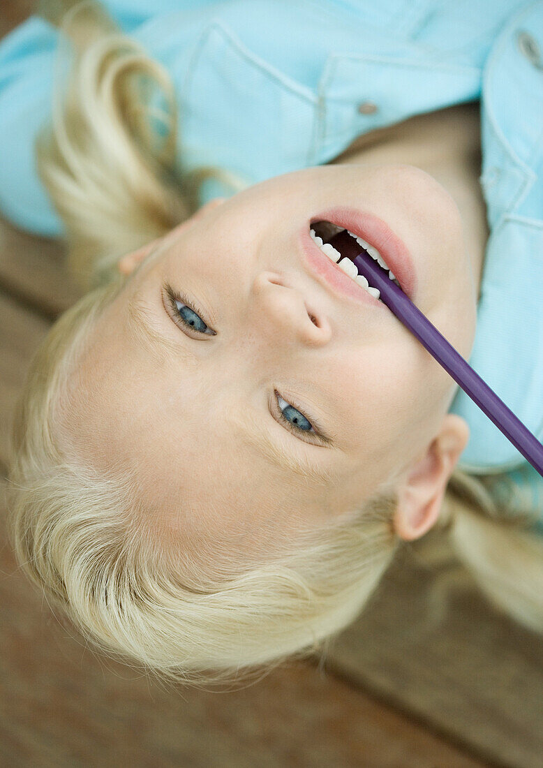 Little girl with head upside down and pencil in mouth