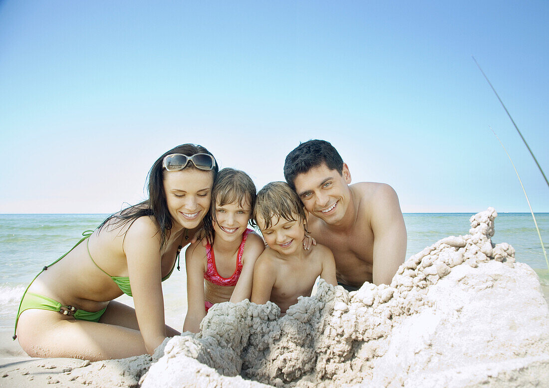 Family sitting on beach near pile of sand, portrait
