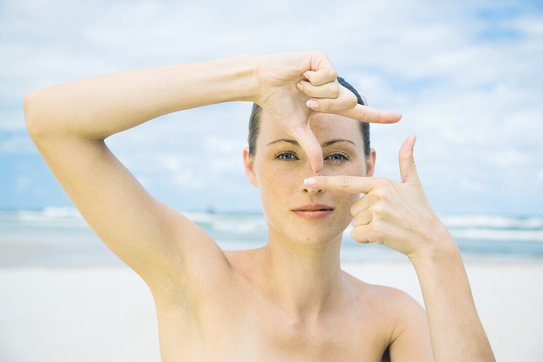 Woman on beach making finger frame around eye, head and shoulders