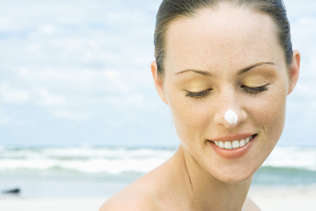 Frau am Strand mit Sonnenschutzmittel auf Nase, Kopf und Schultern