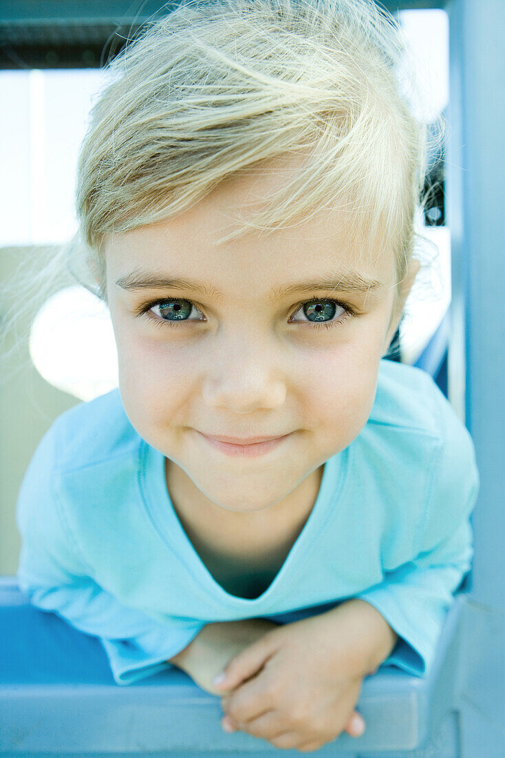 Girl on playground equipment, smiling at camera, portrait