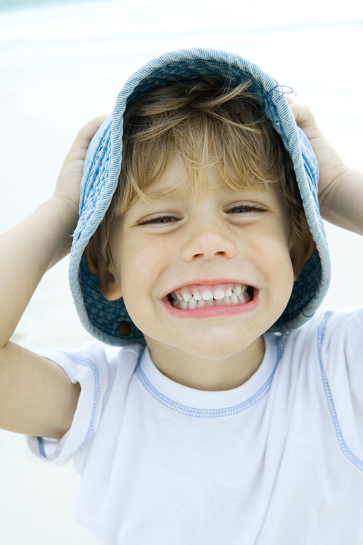 Boy holding hat and smiling on beach, portrait