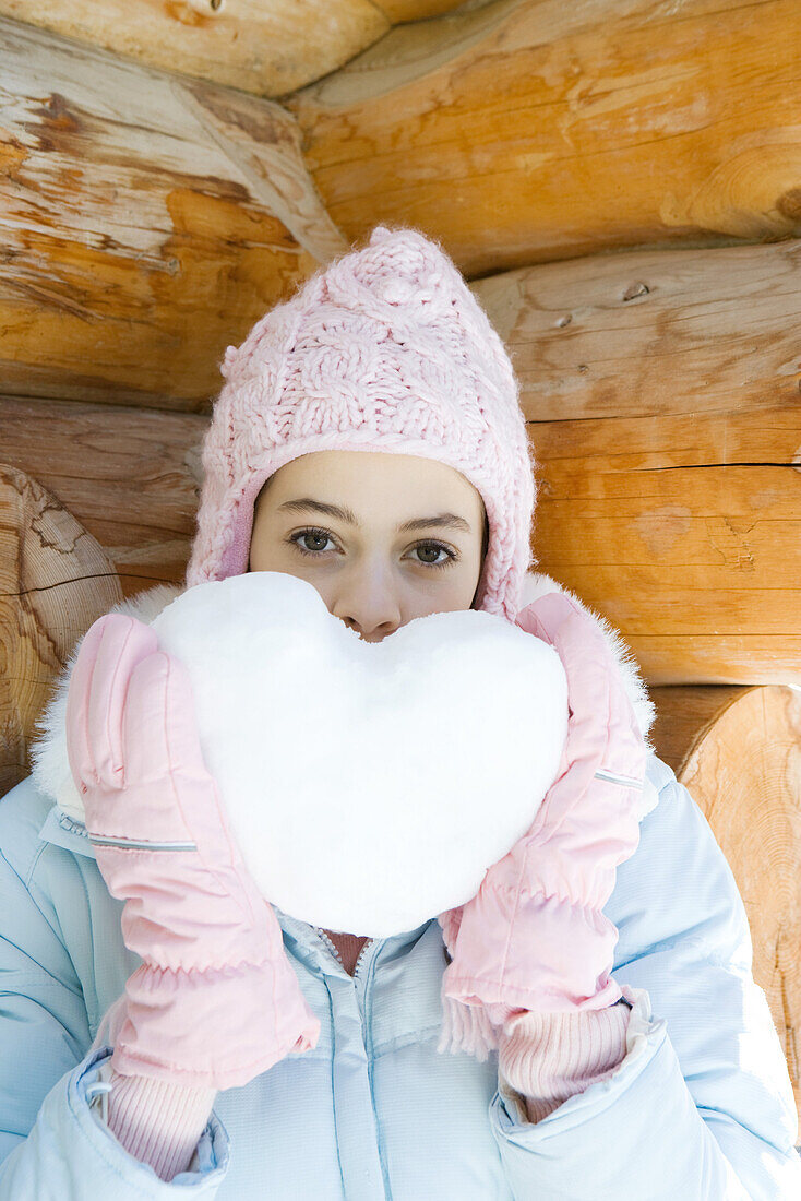 Preteen girl holding up heart made of snow, portrait