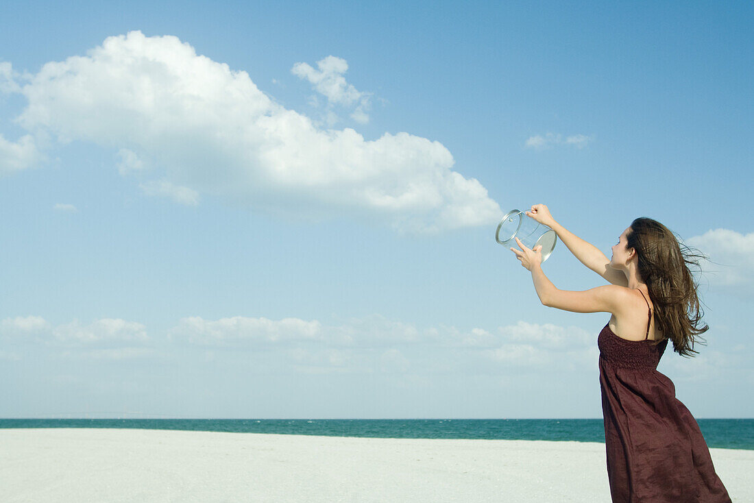 Woman standing on beach, holding up clear container, releasing clouds, optical illusion