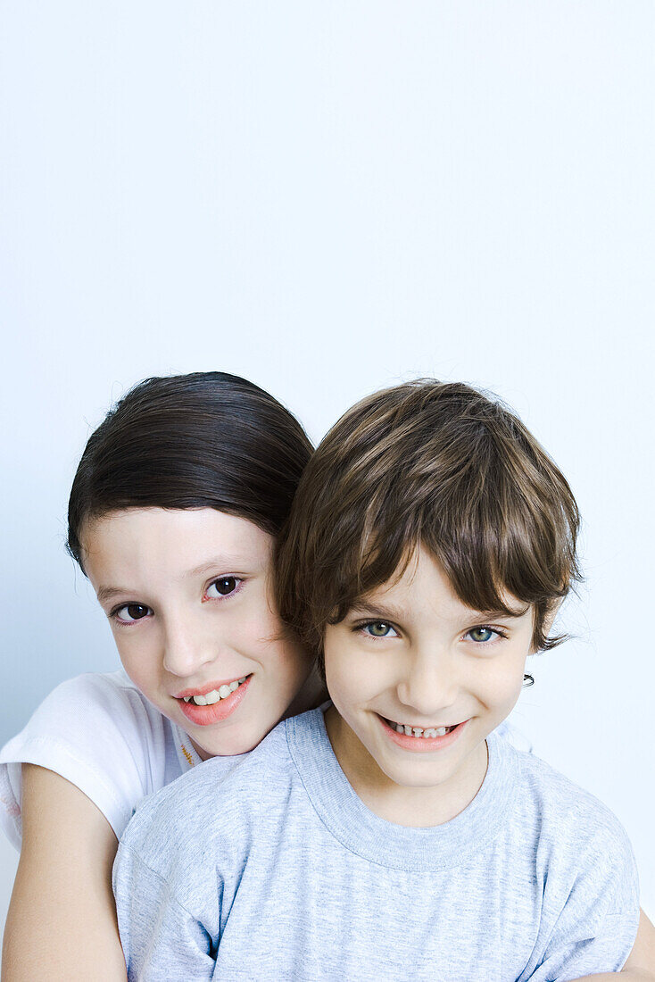Sister hugging her brother from behind, smiling at camera, portrait