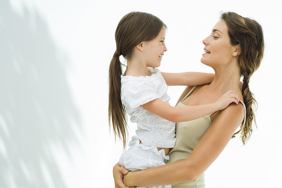 Mother holding and embracing daughter, both smiling at each other, side view