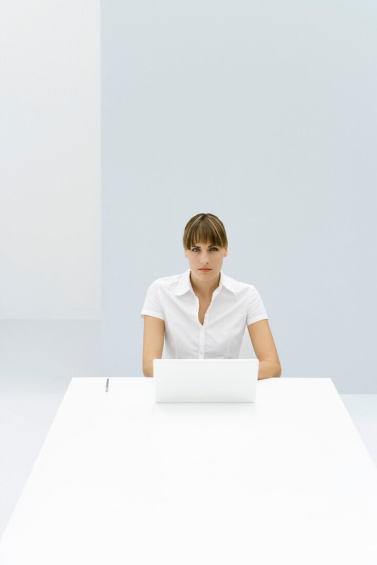 Woman sitting at table with laptop, looking at camera