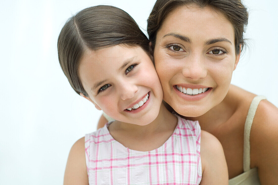 Mother and daughter cheek to cheek, both smiling at camera