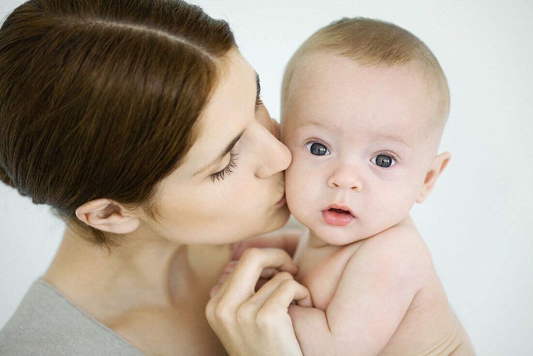 Mother kissing infant on the cheek, baby looking at camera