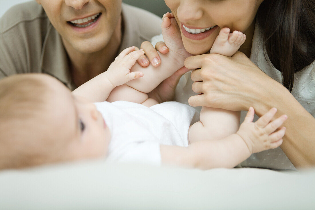 Eltern lächeln auf ihr Baby herab, Mutter hält die Füße des Babys, Ausschnitt