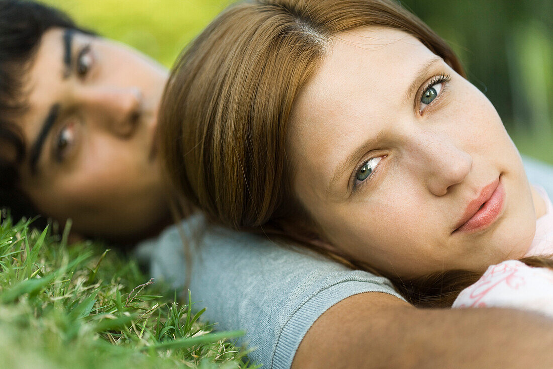 Young couple lying on grass, looking at camera, close-up