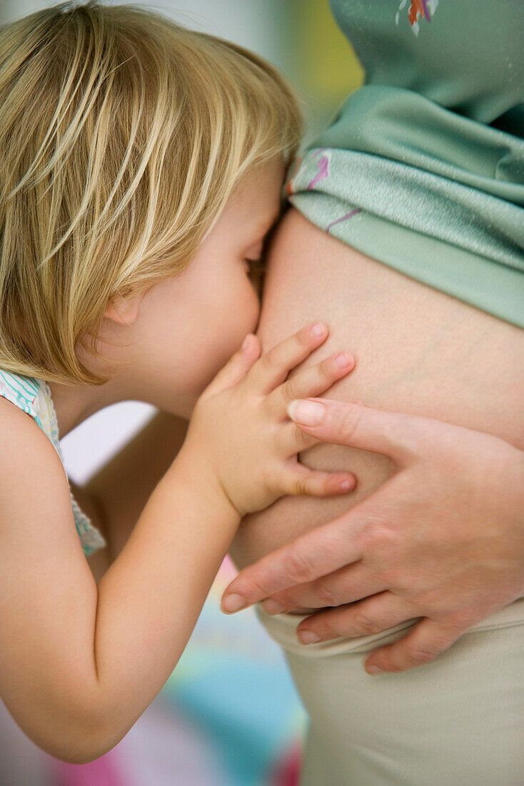 Little girl kissing mother's pregnant belly
