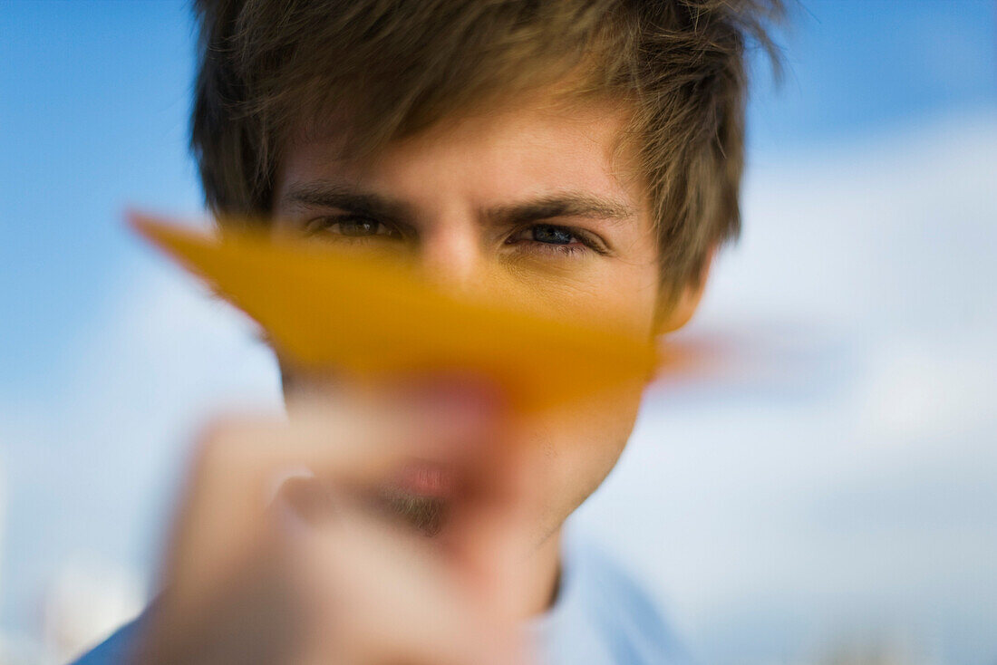 Young man aiming paper airplane at camera