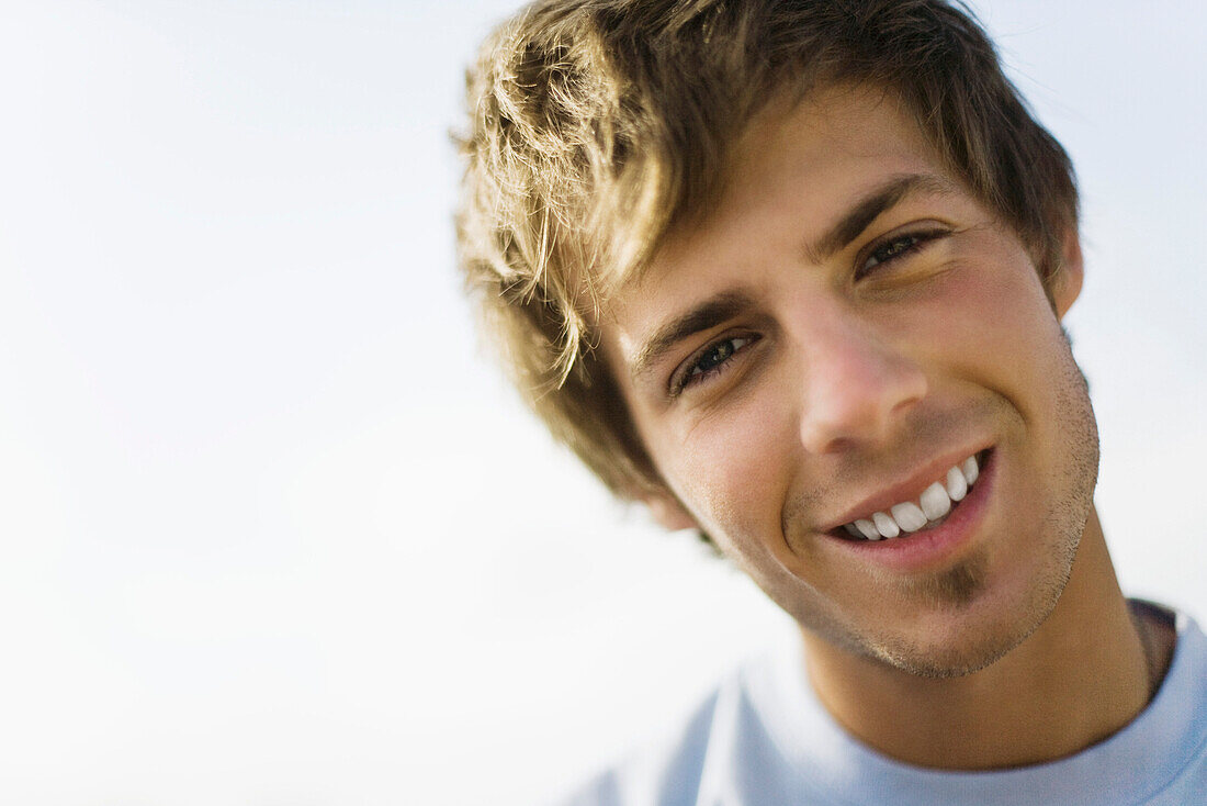 Young man smiling at camera with head tilted, portrait