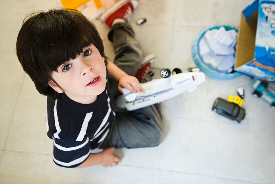 Little boy sitting on floor playing with toys, looking up at camera