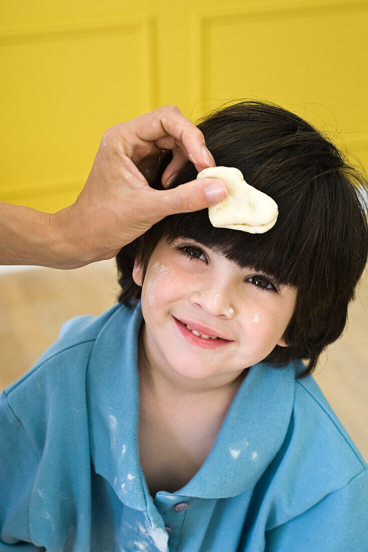 Parent holding dough against little boy's head, cropped