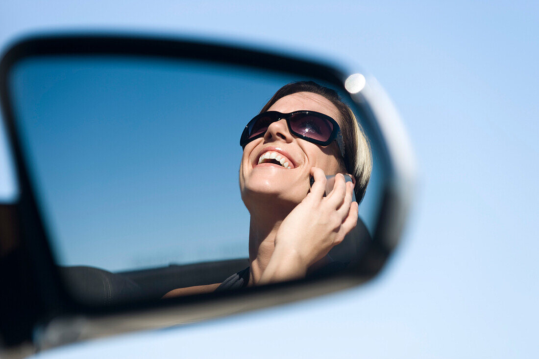 Woman talking on cell phone, reflection in side-view mirror