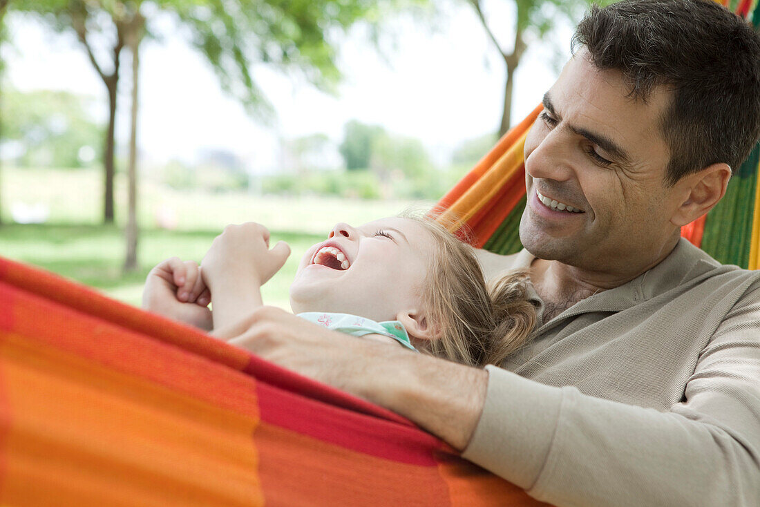 Father and daughter relaxing together in hammock, both laughing