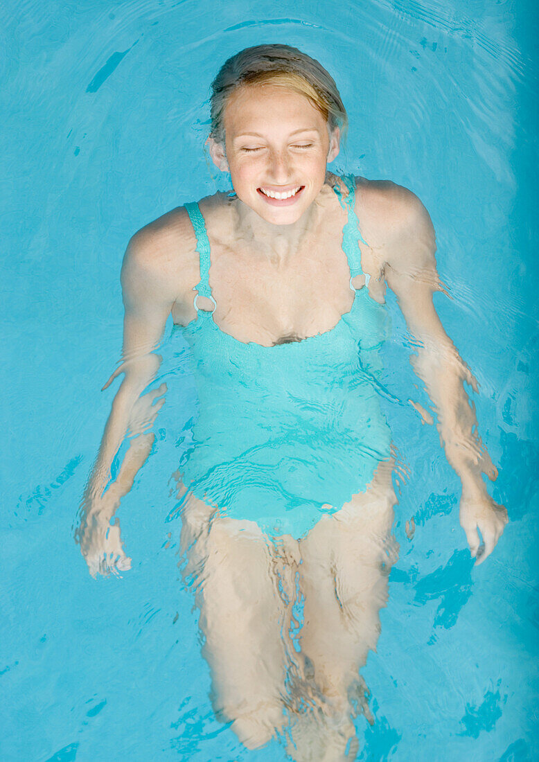 Young woman floating on back in pool, eyes shut