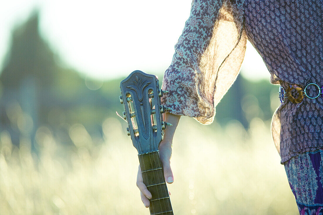 Young hippie woman holding guitar, cropped view of mid section