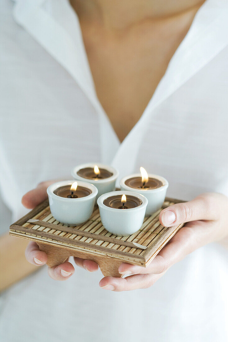 Woman holding tray of candles, close-up, cropped
