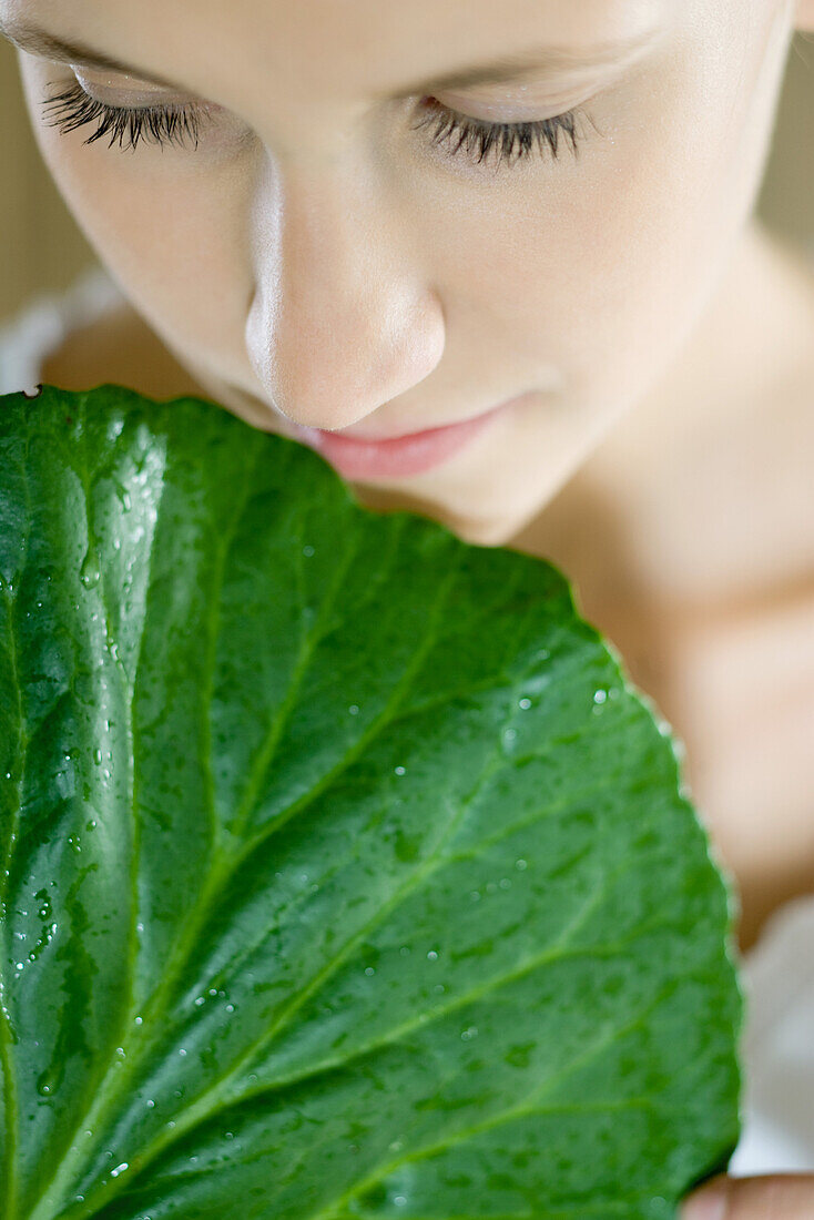 Young woman holding leaf up to face, close-up, cropped