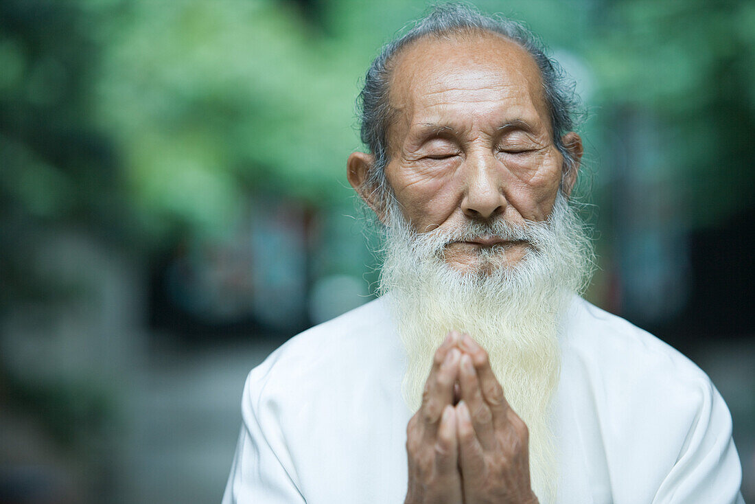 Elderly man in traditional Chinese clothing, hands clasped in prayer