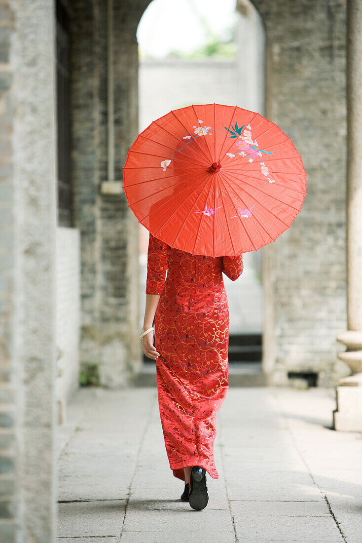 Young woman dressed in traditional Chinese clothing walking with parasol, rear view