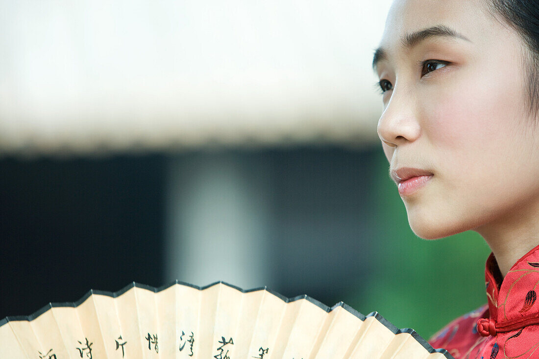 Young woman dressed in traditional Chinese clothing holding fan, cropped view