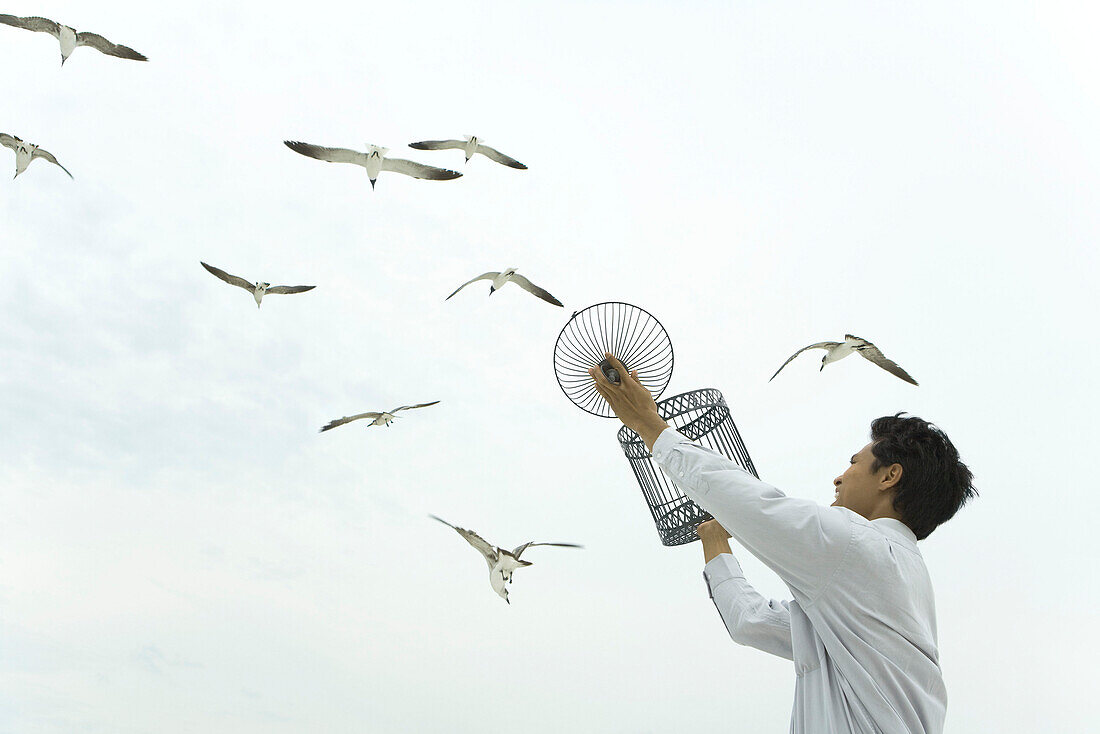 Man holding up bird cage, releasing bird, gulls souring overhead