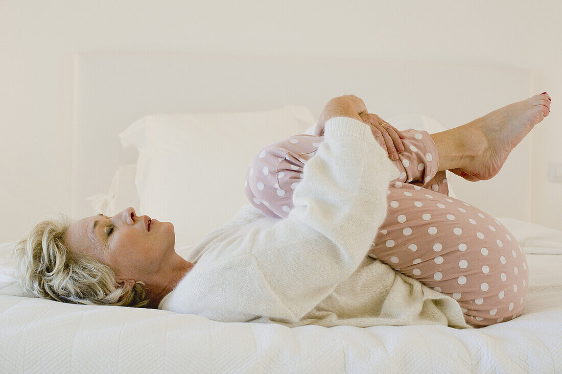 Ältere Frau auf dem Bett liegend in Fötusstellung