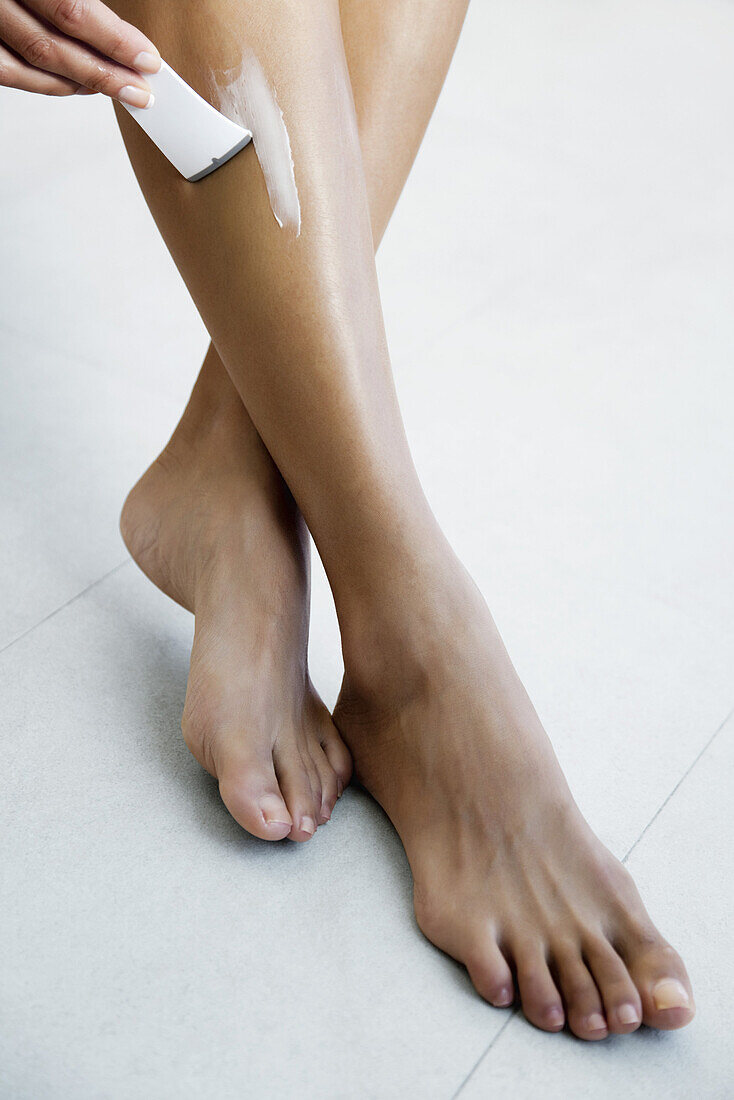 Woman applying hair removal cream to leg