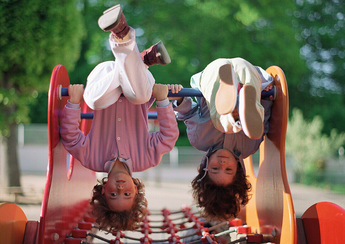 Two children hanging upside down on jungle gym