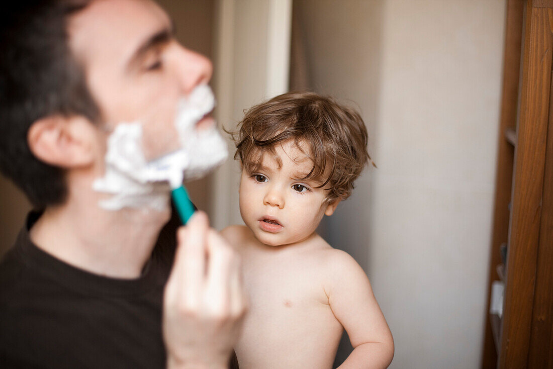 Toddler boy watching his father shave