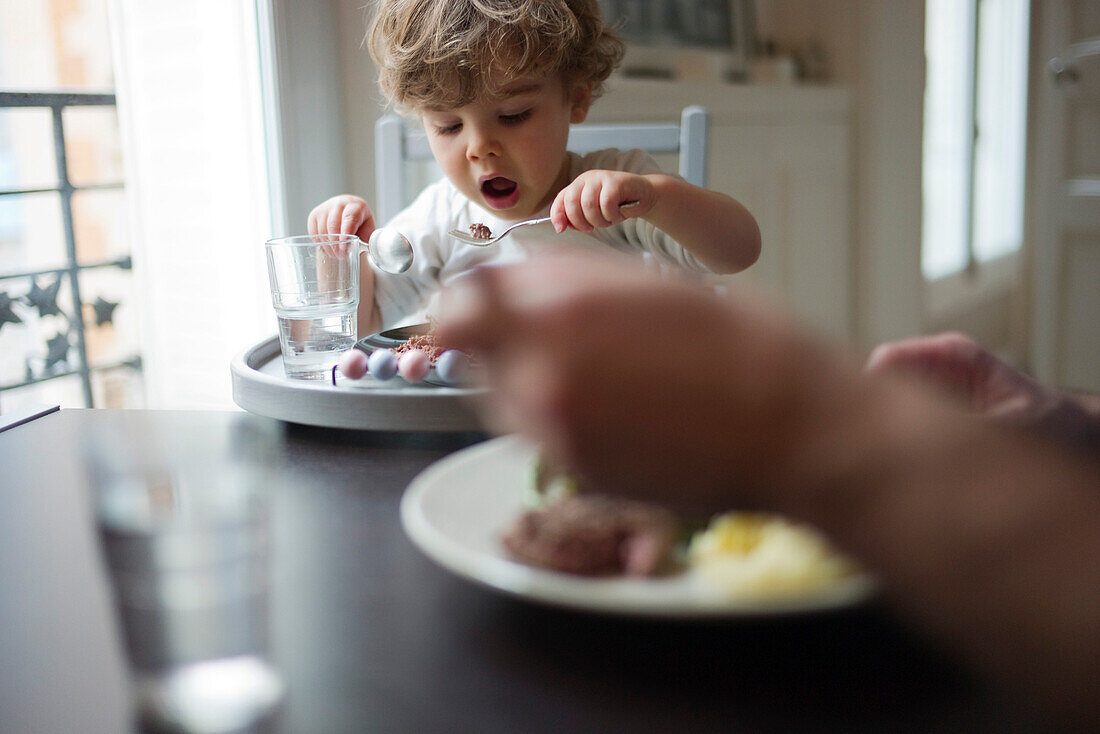 Toddler boy eating meal with parent