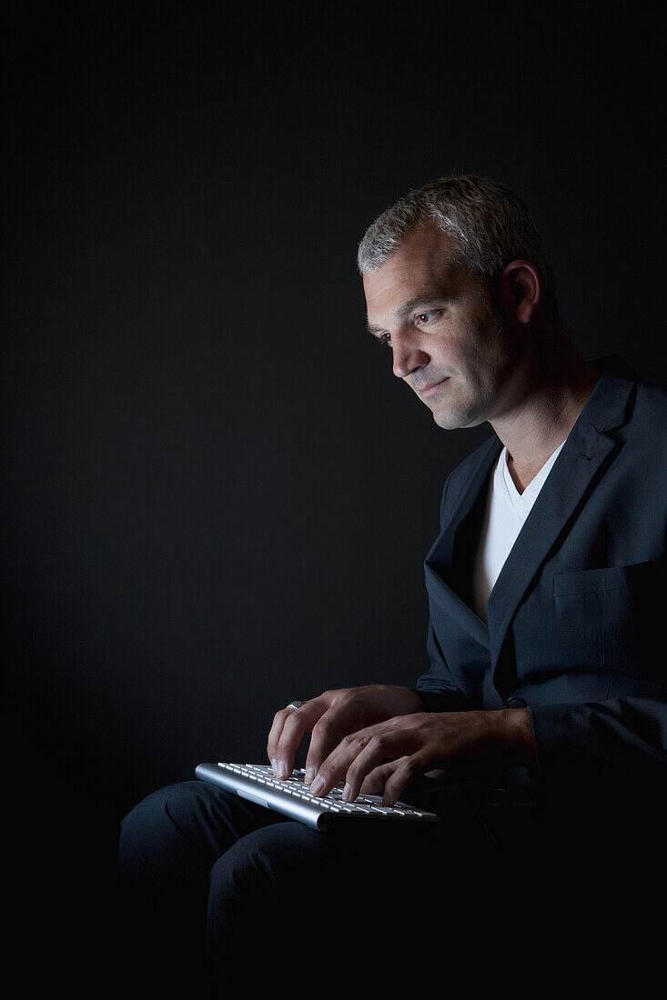 A businessman typing on a computer keyboard in the dark