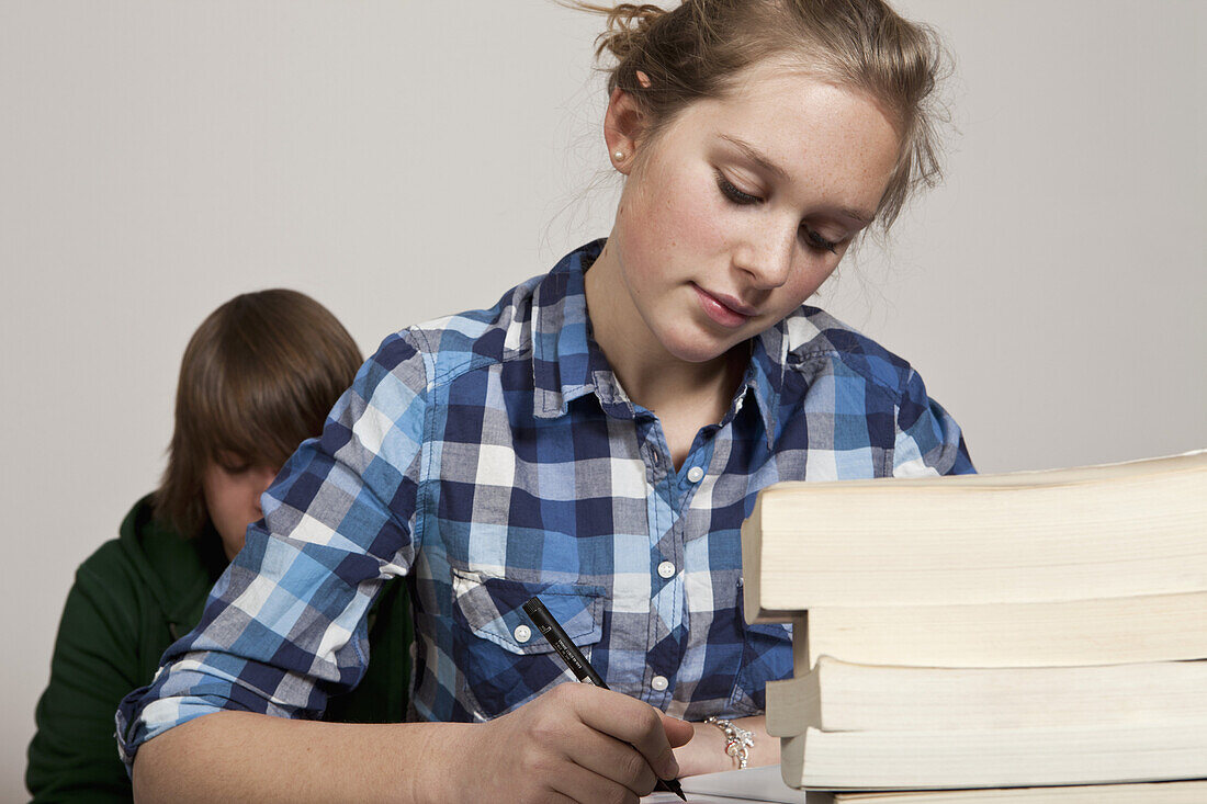 A teenage girl doing class work, boy in background