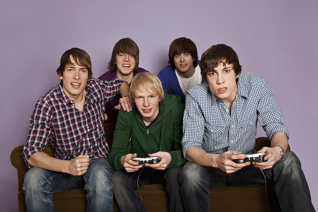 Two teenage boys playing a video game while their friends cheer them on