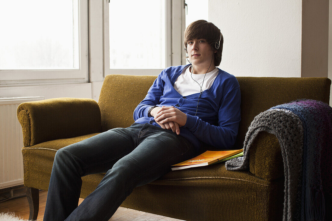 A teenage boy wearing headphones sitting on a couch