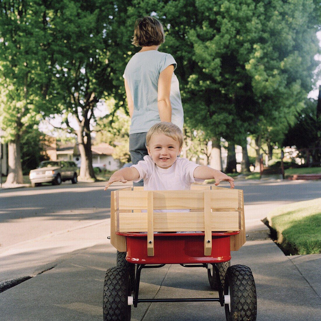 A mother pulling her young son in a wagon, focus on boy