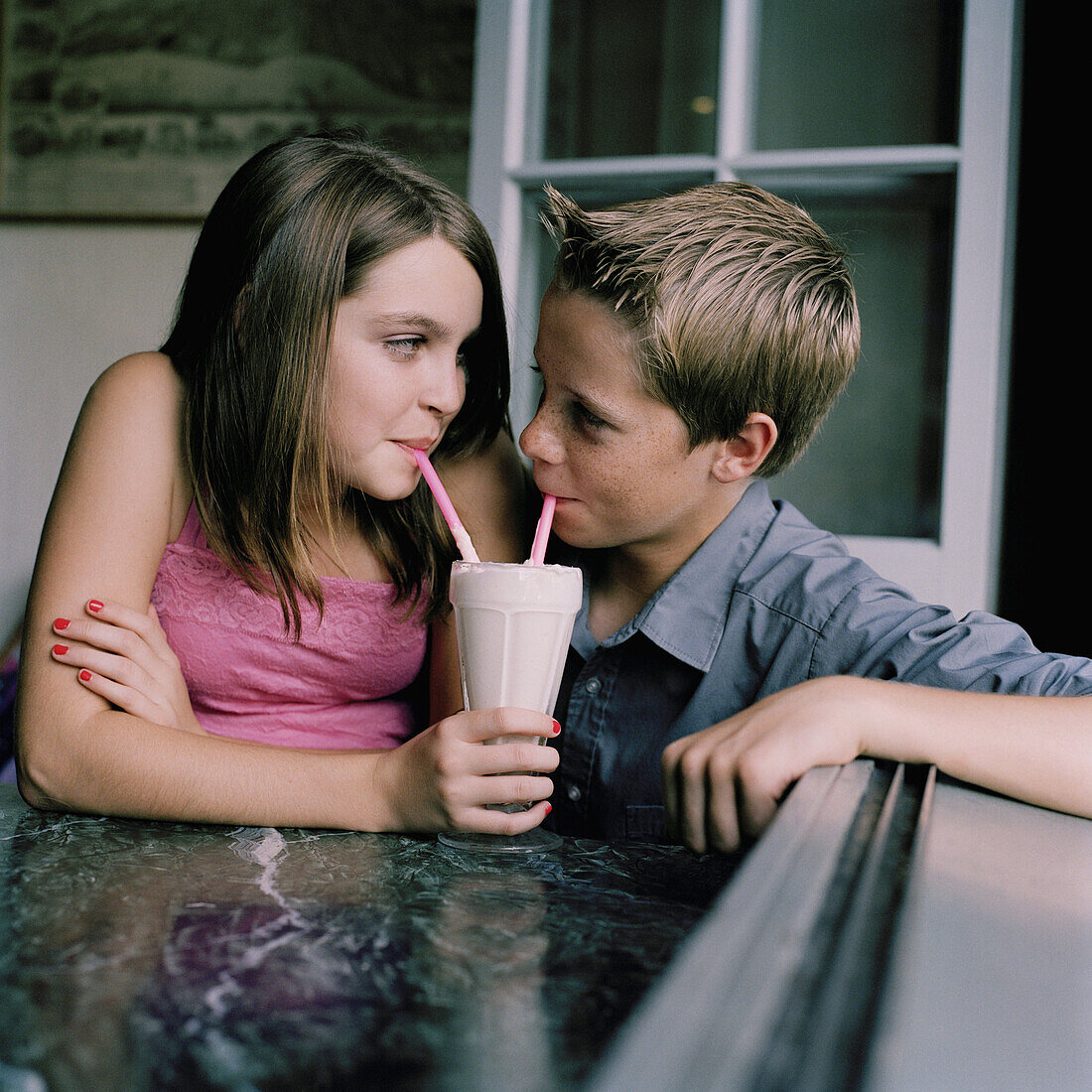 A young teenage couple sharing a milkshake at a diner