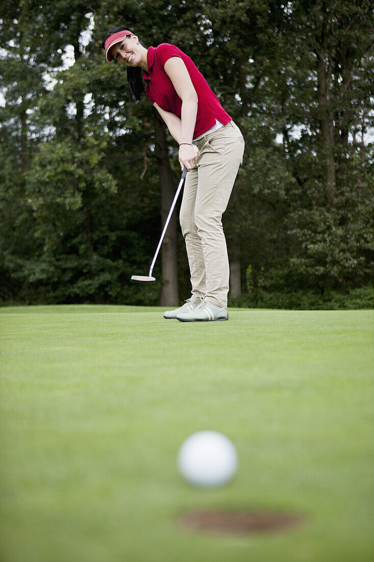 A female golfer putting, golf ball at edge of hole