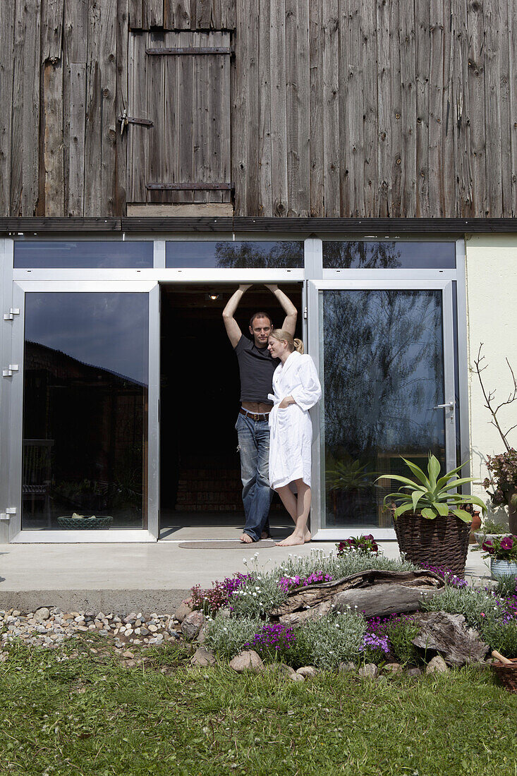 A couple leaning against the doorway of their house in the morning