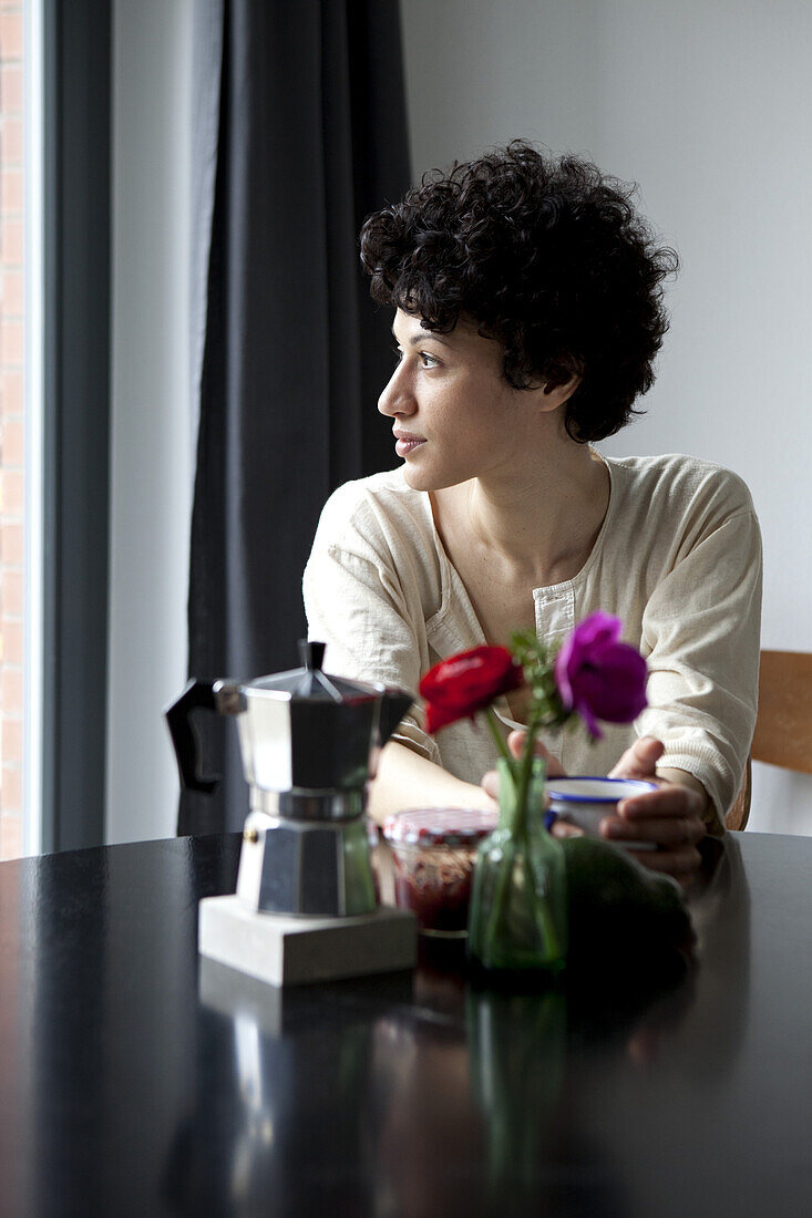 A woman sitting at a table looking thoughtfully out of a window