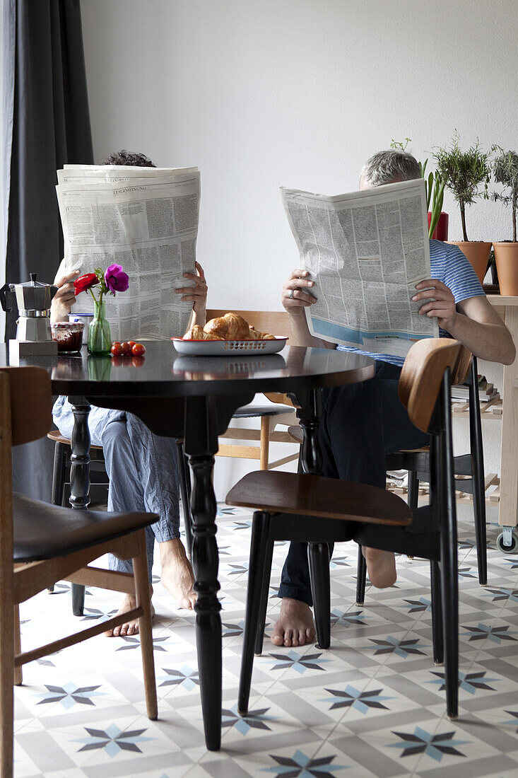 A mixed age couple reading newspapers at the breakfast table